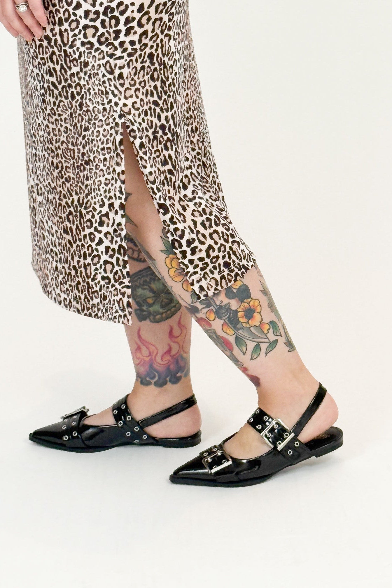 Person wearing leopard print skirt and black sandals with floral tattoos on a white background