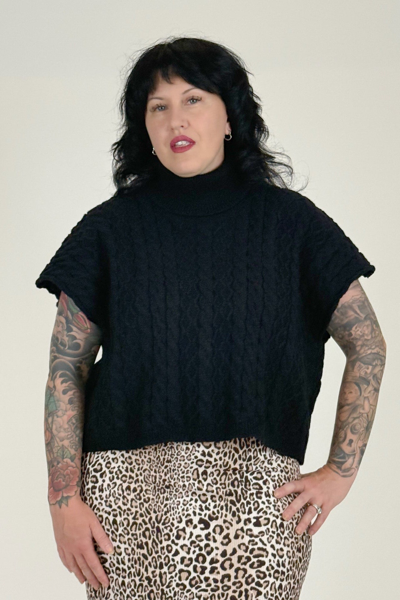 Woman wearing a black turtleneck sweater and leopard print pants on a plain background
