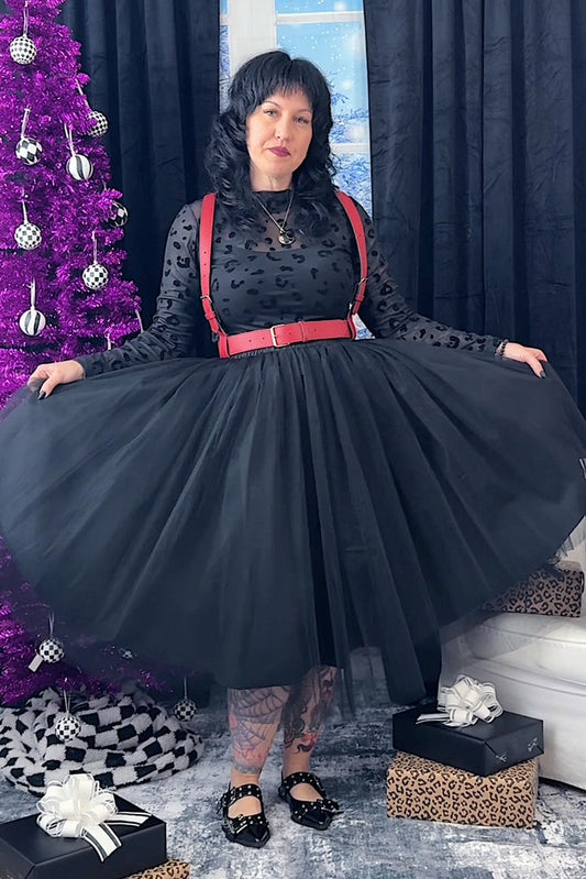 Woman in a black tulle skirt with red harness standing next to a decorated Christmas tree.