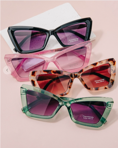 Four pairs of sunglasses with different frame designs and colors on a light pink background.