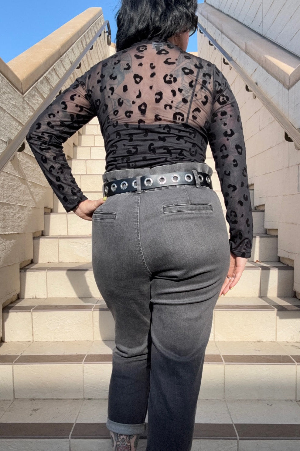 Person wearing a sheer leopard print top and gray jeans on stone steps.