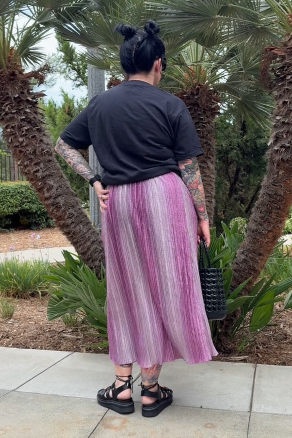 Person wearing a black shirt and pink skirt standing in front of palm trees.