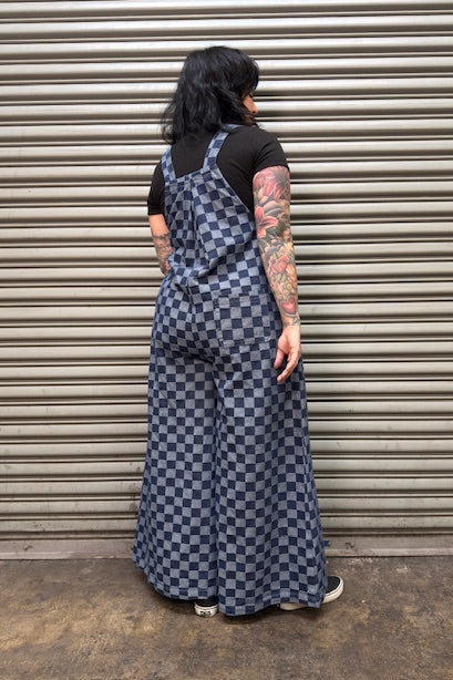 Person wearing a checkered denim overalls standing in front of a metal shutter.