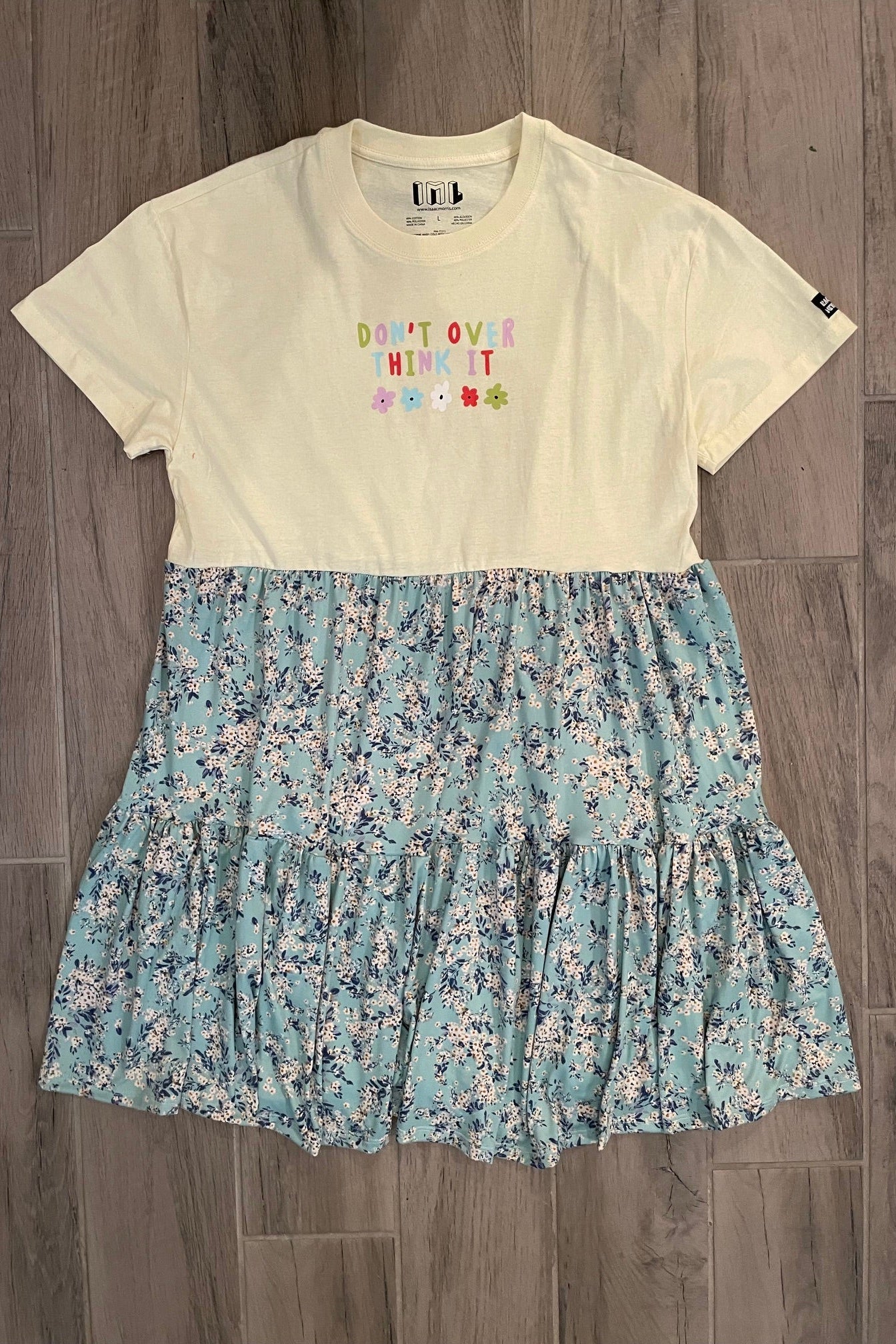 A t-shirt dress with a floral skirt and solid yellow top, laid flat on a wooden surface.
