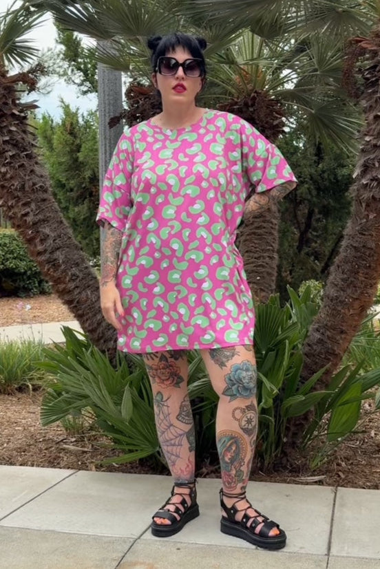 Person wearing a pink dress with green patterns standing outdoors with palm trees in the background