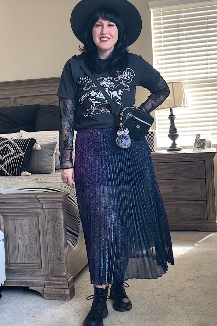 Person wearing a black outfit with a hat, top, skirt, and boots in a room.