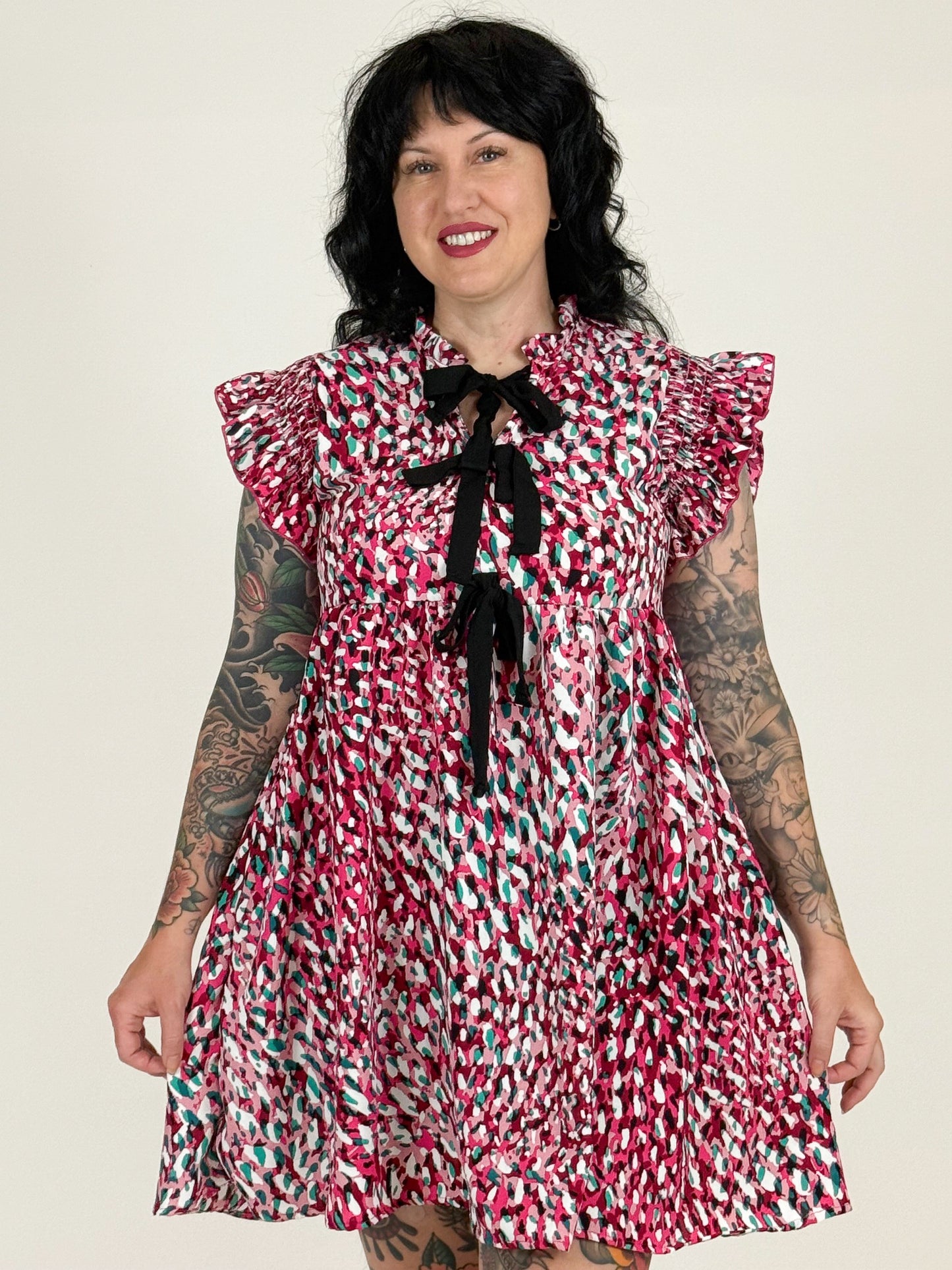 Woman wearing a colorful patterned dress with ruffled sleeves against a plain background