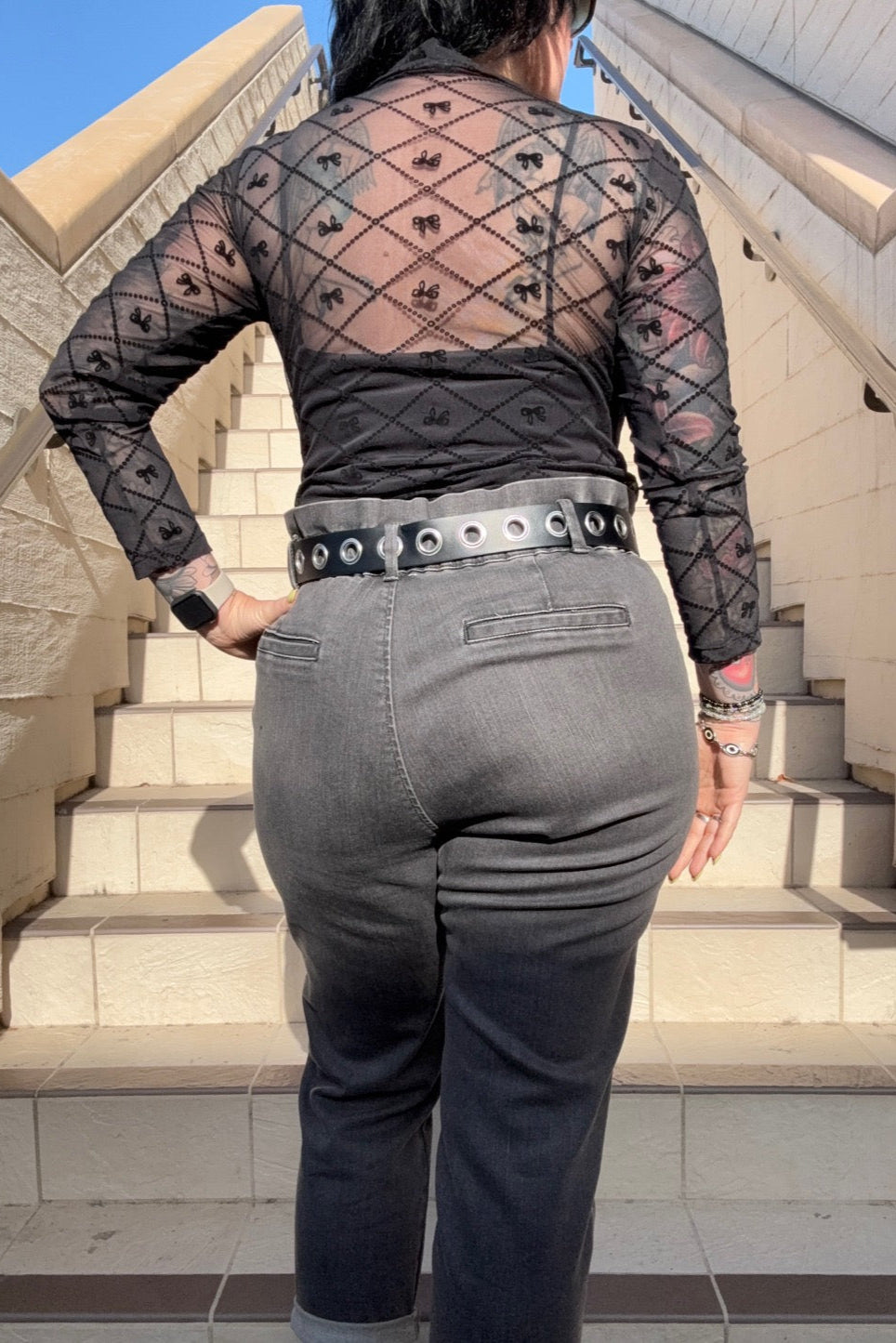 Person wearing a sheer black top and gray pants on stone steps.