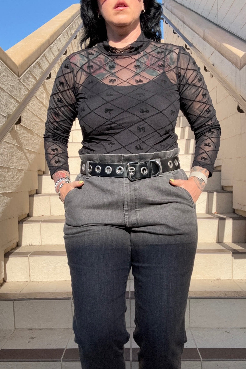 Person wearing a black patterned top and gray pants on stone steps.