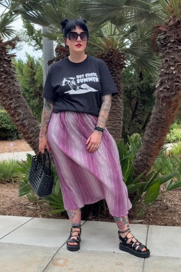 Person wearing a black t-shirt and pink skirt standing in front of palm trees.