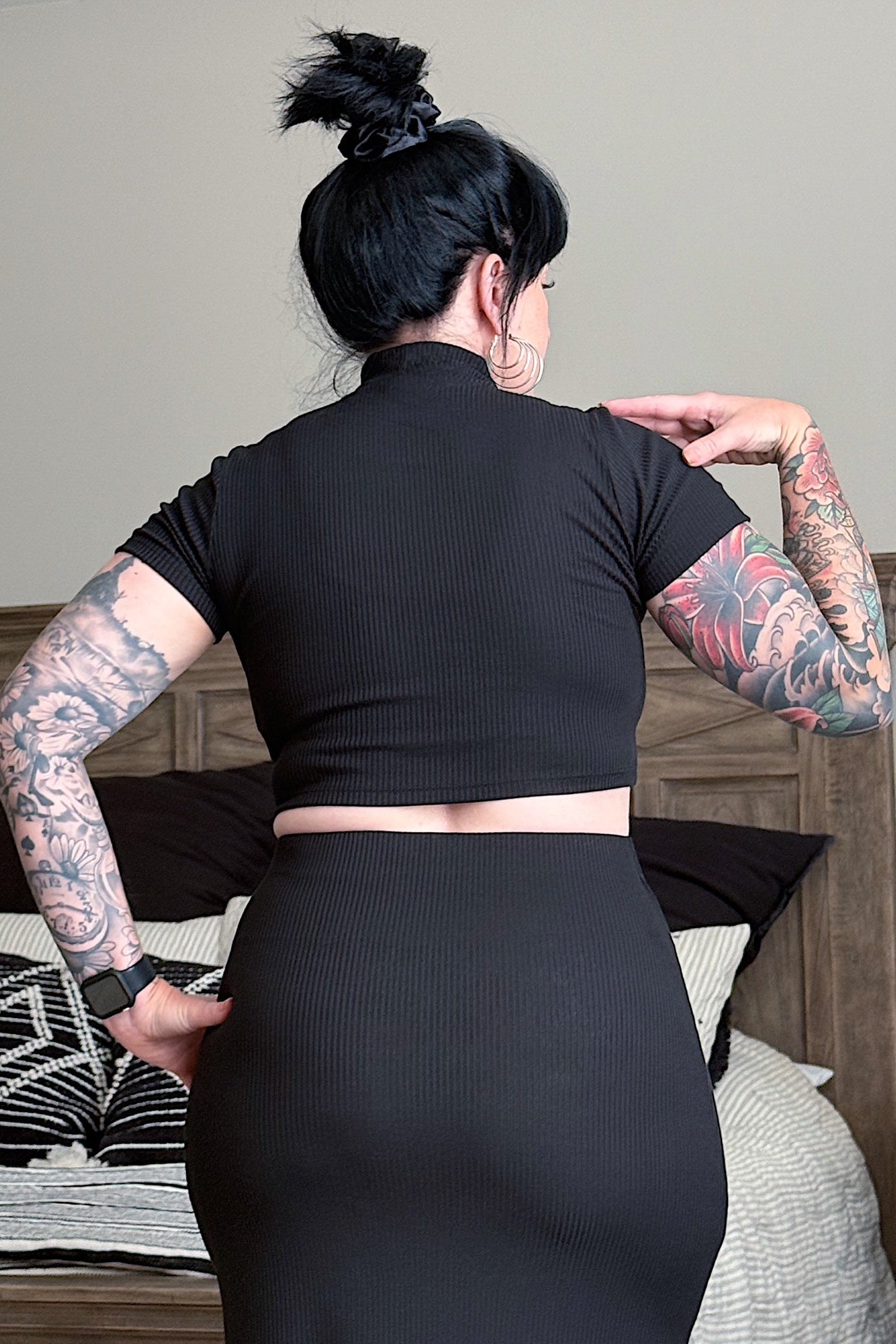 Person wearing a black outfit standing in a bedroom.