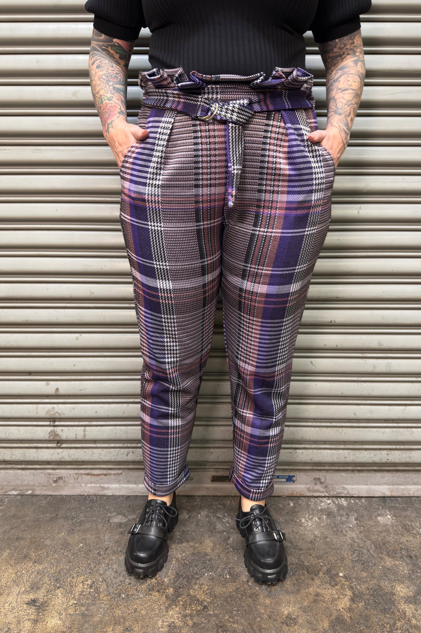 Person wearing plaid pants standing in front of a metal shutter.