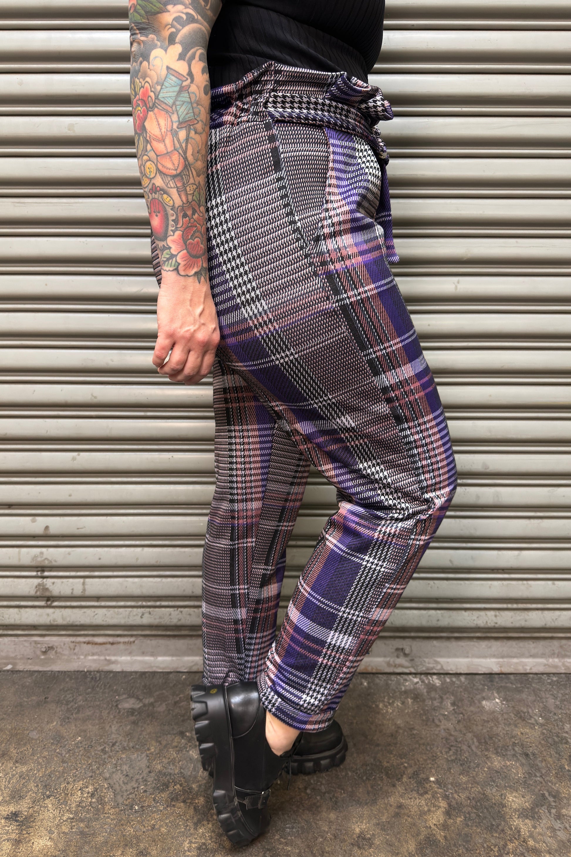 Person wearing plaid pants standing in front of a metallic shutter.