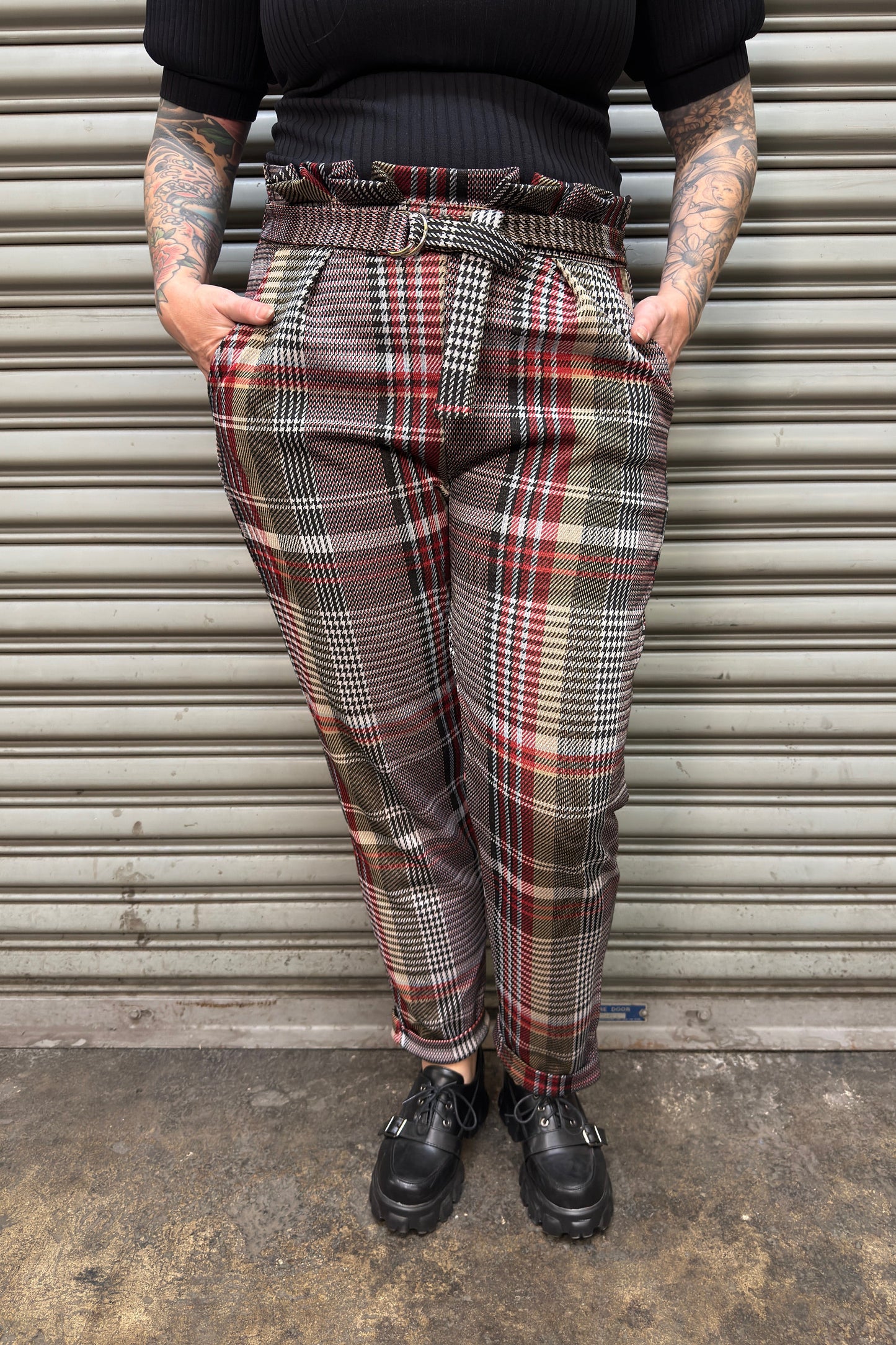 Person wearing plaid pants standing in front of a metal shutter.