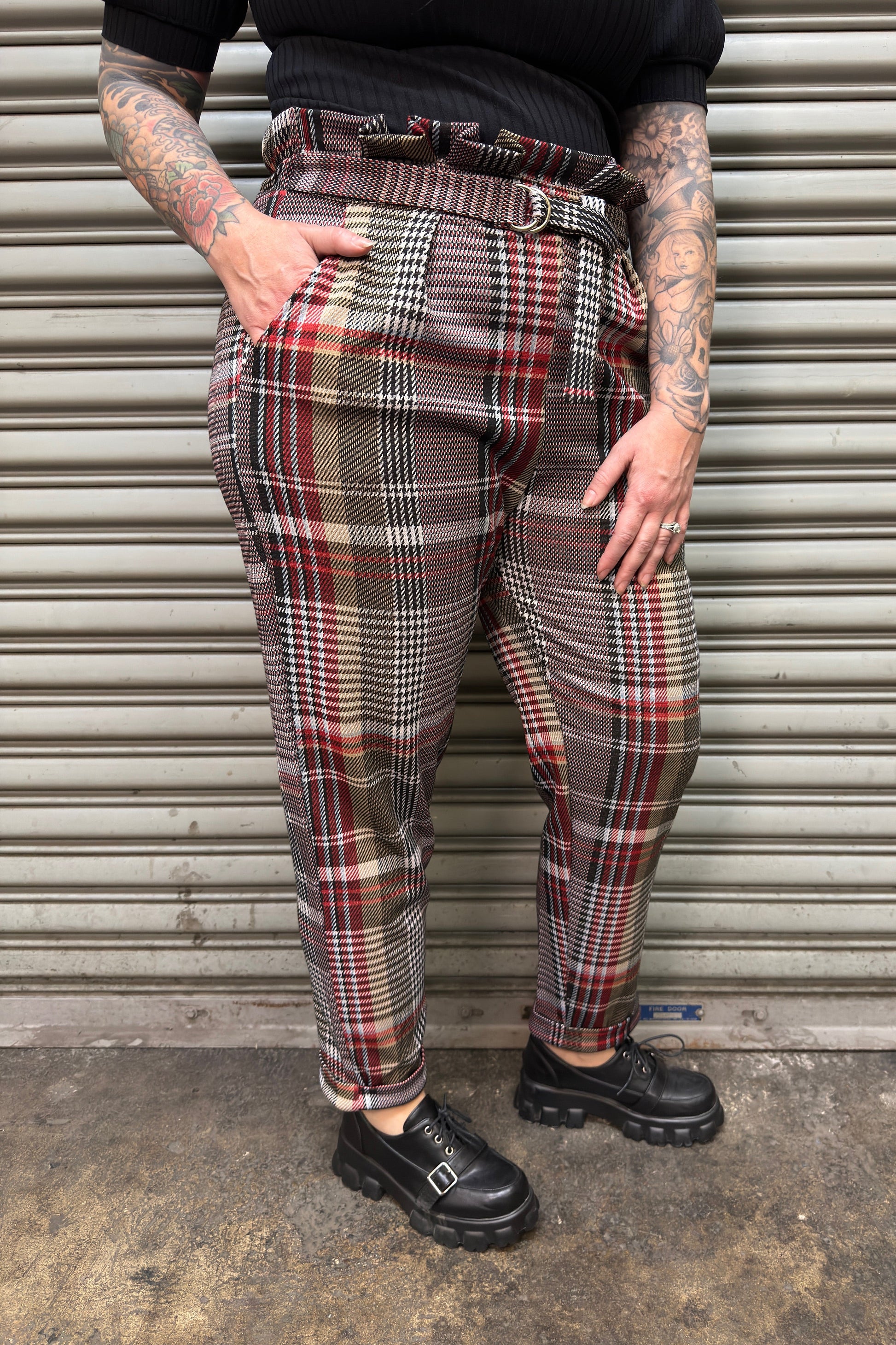 Person wearing plaid pants and black shoes standing in front of a metallic shutter.