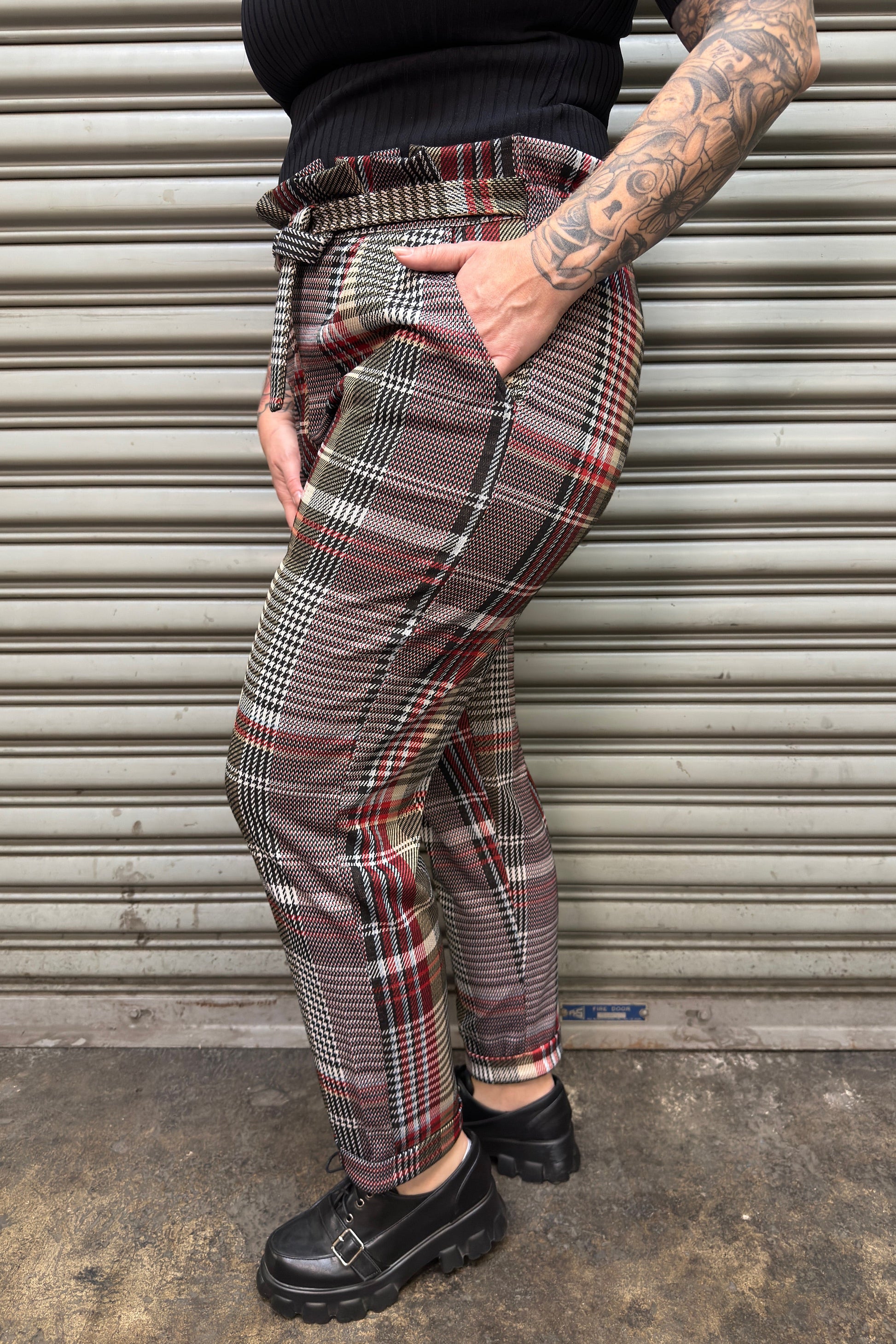 Person wearing plaid pants and black shoes standing against a metallic shutter.