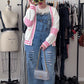 Person wearing a checkered jacket, denim overalls, and sunglasses in a clothing store.