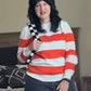 Person wearing a red and white striped sweater and black skirt in a bedroom.