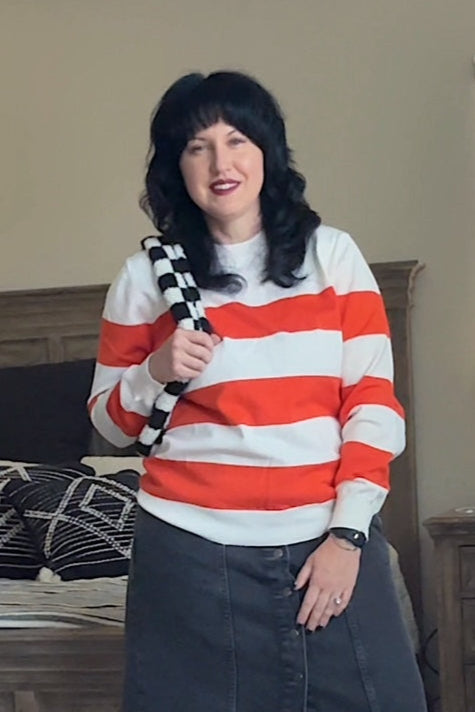 Person wearing a red and white striped sweater and black skirt in a bedroom.