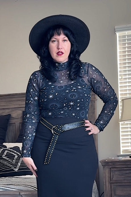 Woman in a dark outfit with a hat standing in a living room.