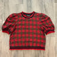 A red and black plaid short-sleeve top laid flat on a gray wood-look floor.