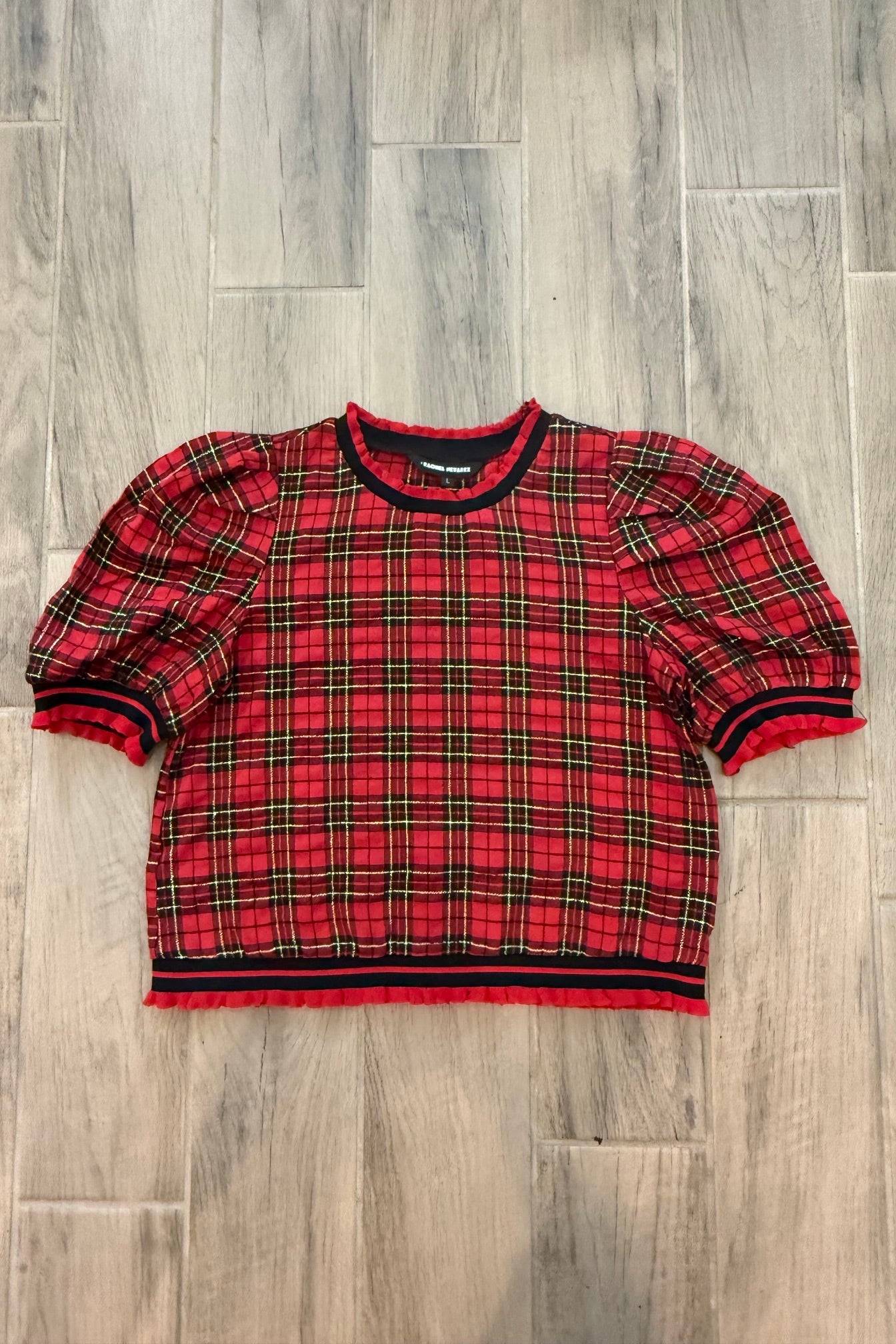 A red and black plaid short-sleeve top laid flat on a gray wood-look floor.