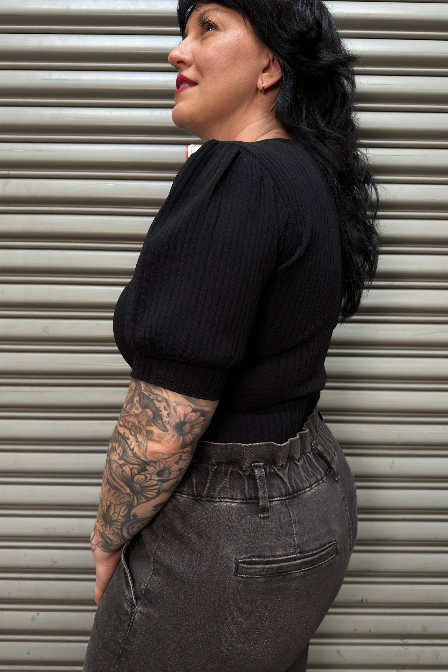 Person wearing a black top and gray pants against a metallic shutter background