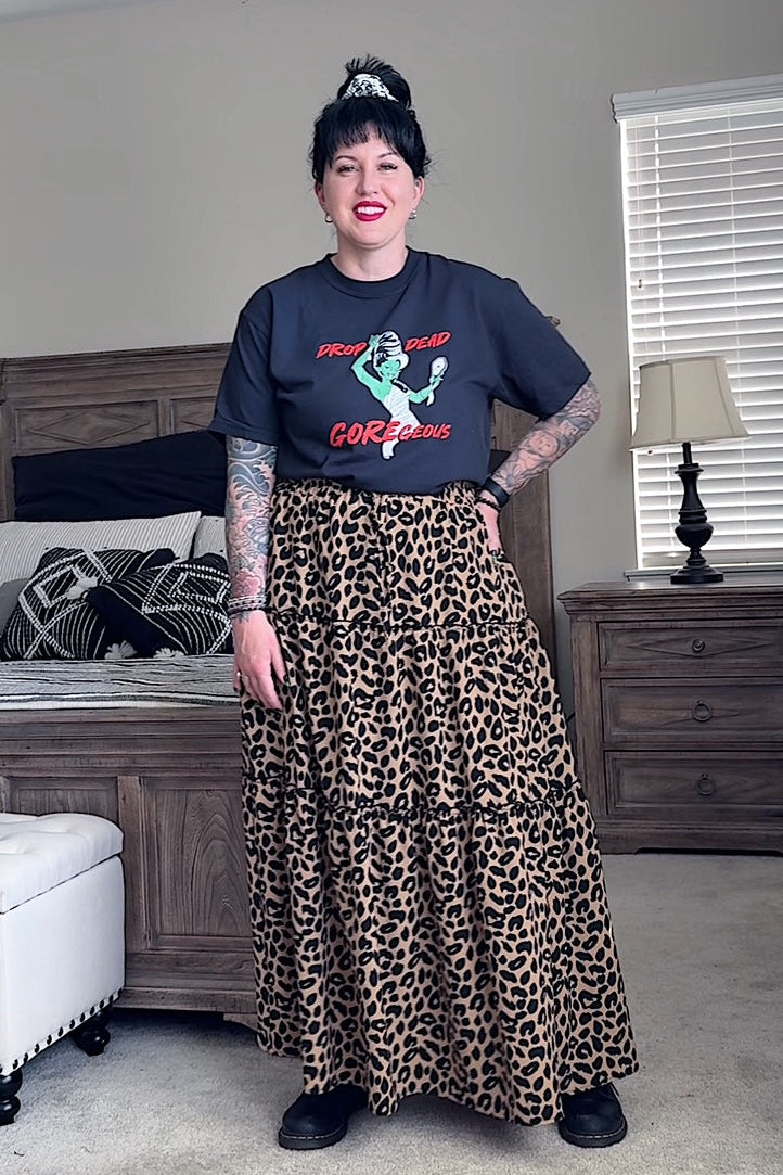 Person wearing a graphic t-shirt and leopard print skirt in a bedroom setting