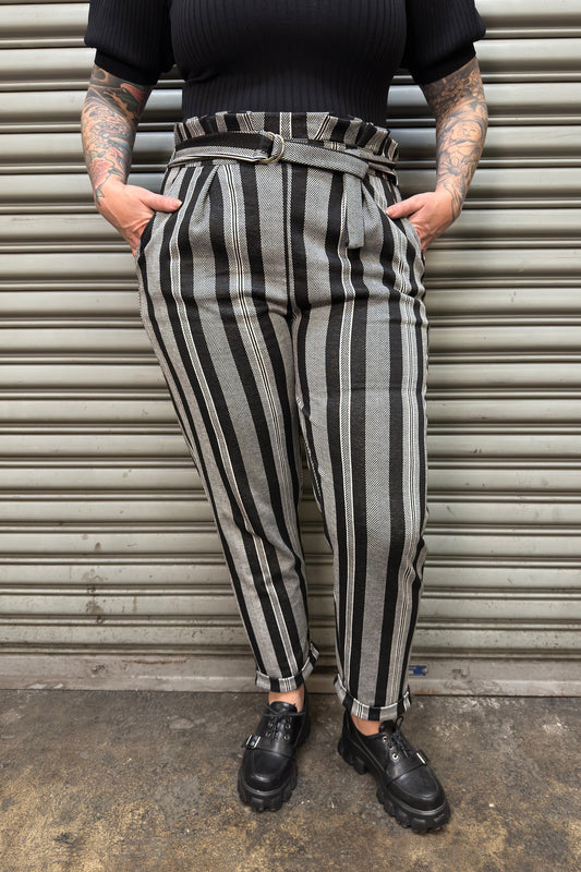 Person wearing black and white striped pants with a textured wall background
