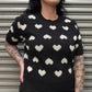 Person wearing a black sweater with white heart patterns against a metallic background