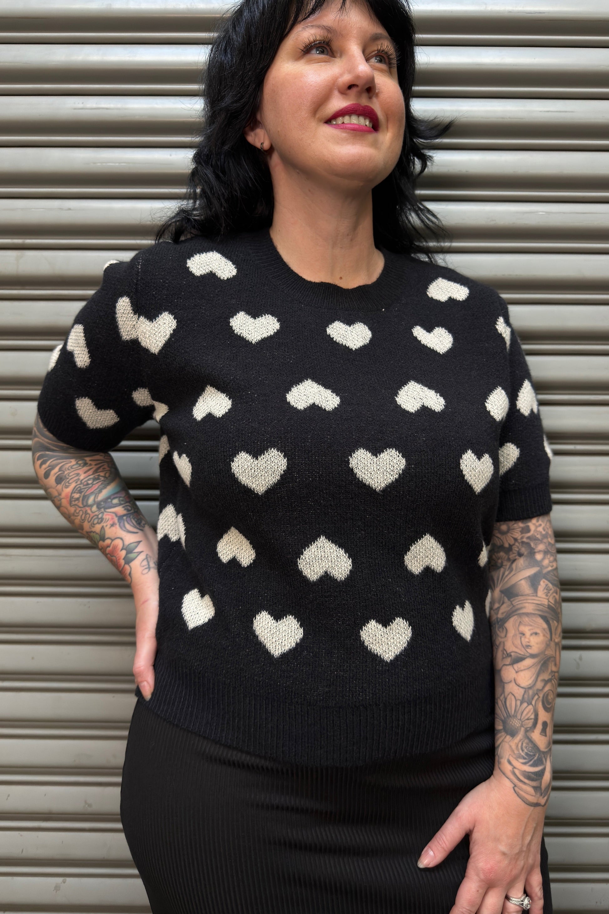 Person wearing a black sweater with white heart patterns against a metallic background