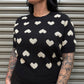 Person wearing a black sweater with white heart patterns against a metallic shutter background