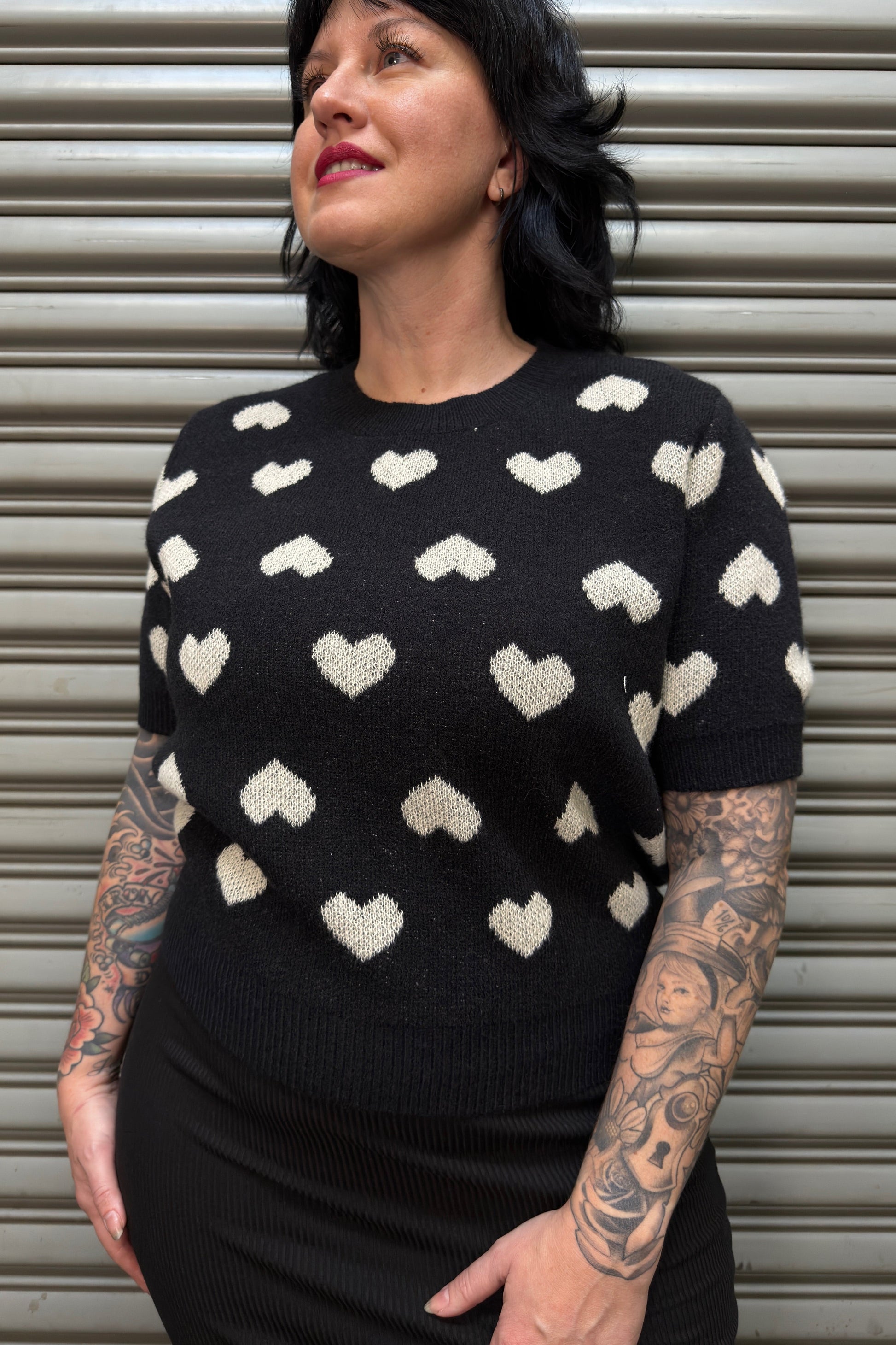 Person wearing a black sweater with white heart patterns against a metallic shutter background
