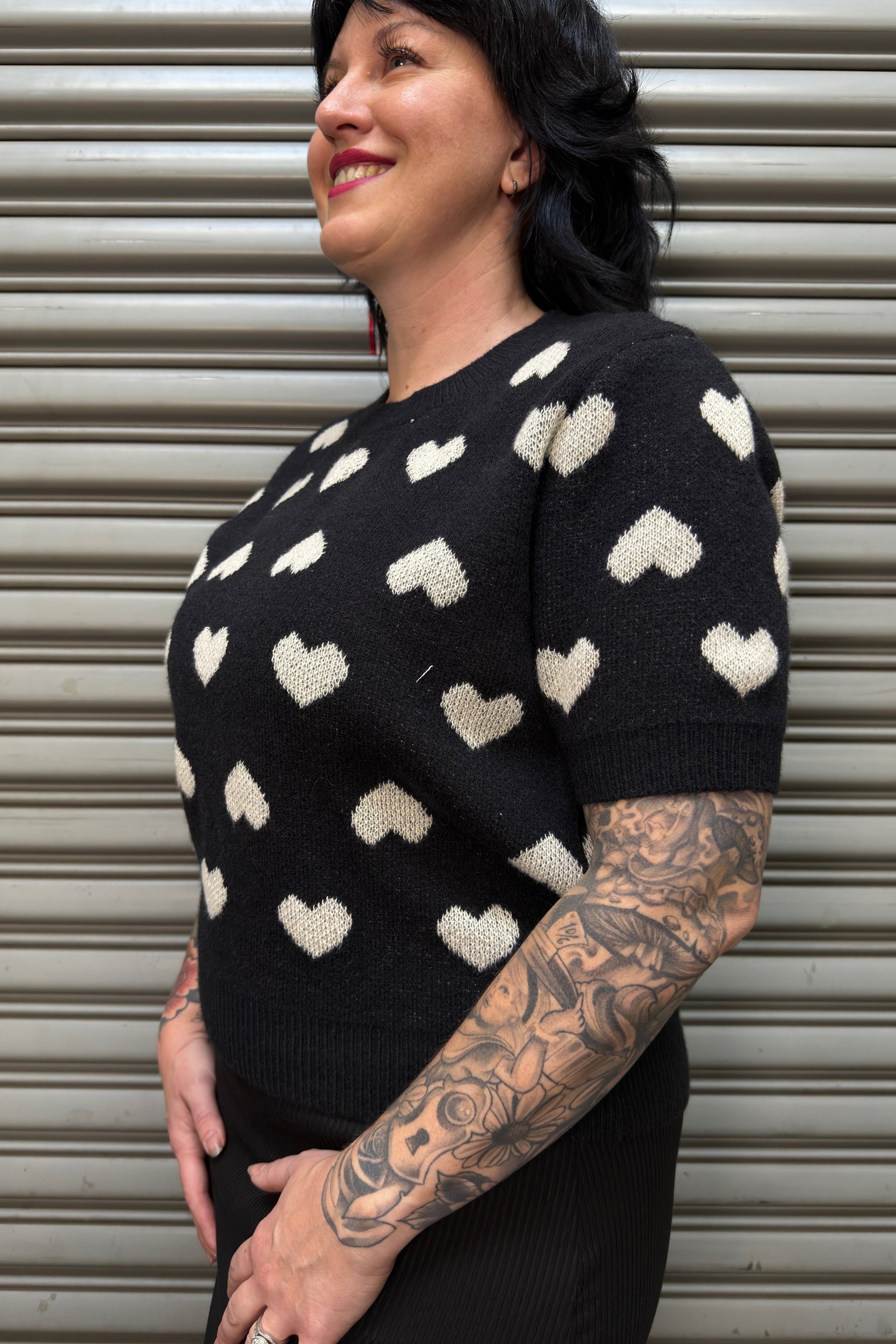 Woman wearing a black sweater with white heart patterns against a metallic shutter background