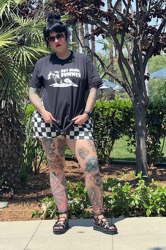 Person wearing a black t-shirt with a graphic design and checkered shorts standing outdoors.