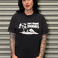 Person wearing a black t-shirt with graphic design and text, standing against a metallic shutter.