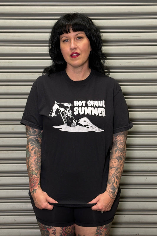 Person wearing a black t-shirt with graphic design and text, standing against a metallic shutter.