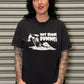 Person wearing a black t-shirt with graphic design and text, standing against a metallic shutter.