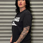 Person wearing a black t-shirt with white text and graphics against a metallic shutter background