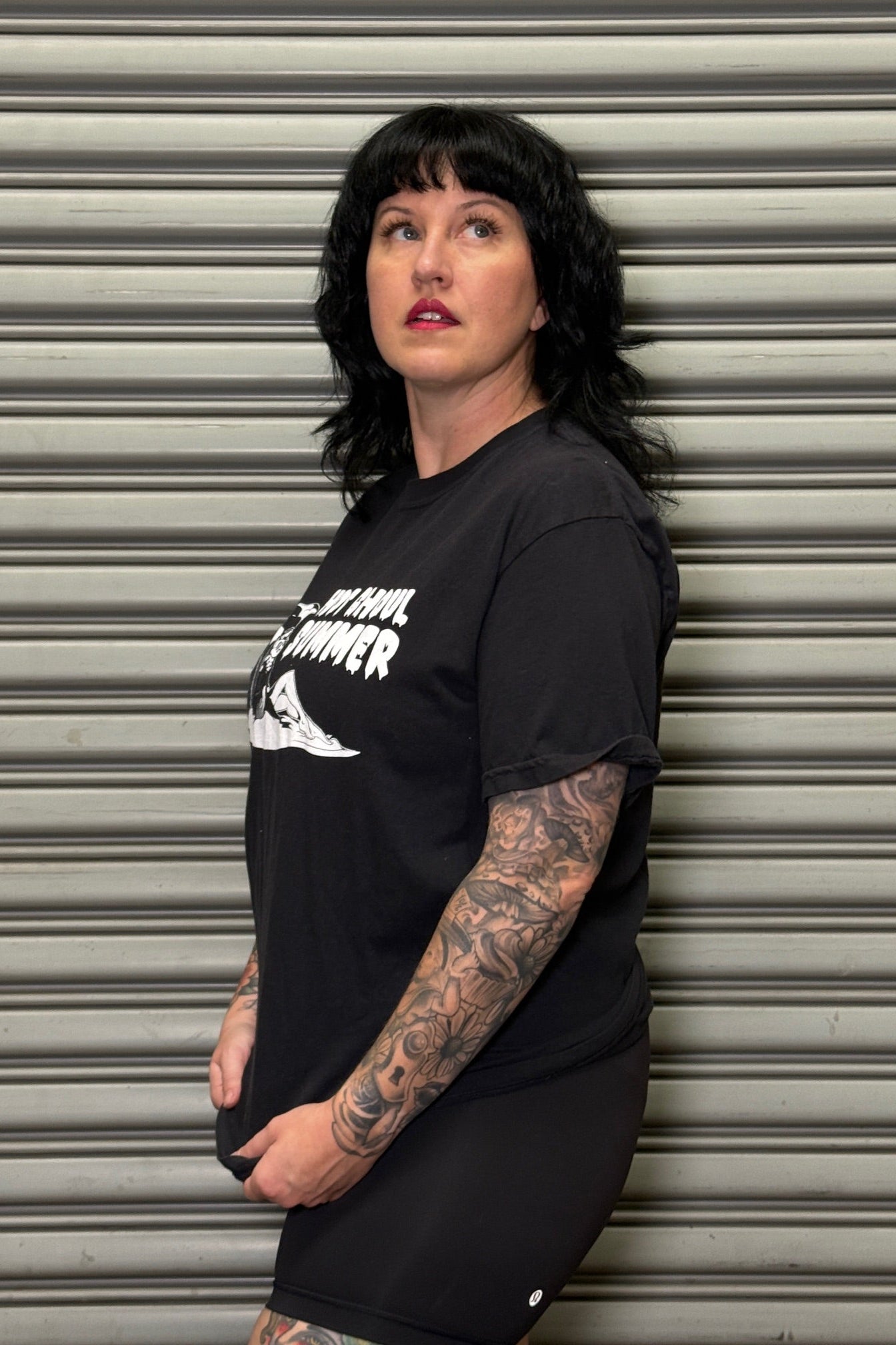 Person wearing a black t-shirt with white text and graphics against a metallic shutter background