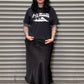 Person wearing a black t-shirt and skirt standing in front of a metal shutter.