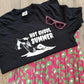 Black tank top with graphic design and sunglasses on a pink and green patterned fabric