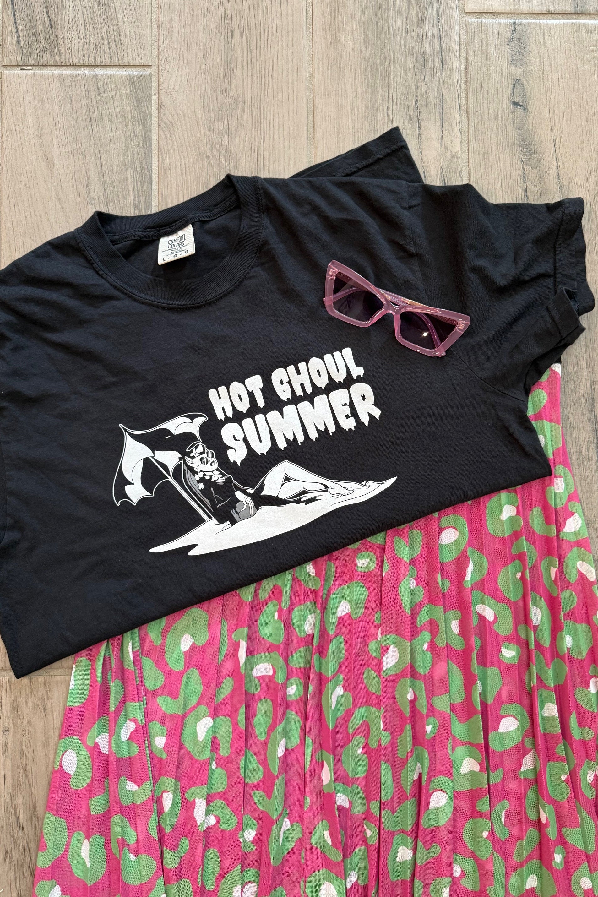 Black tank top with graphic design and sunglasses on a pink and green patterned fabric