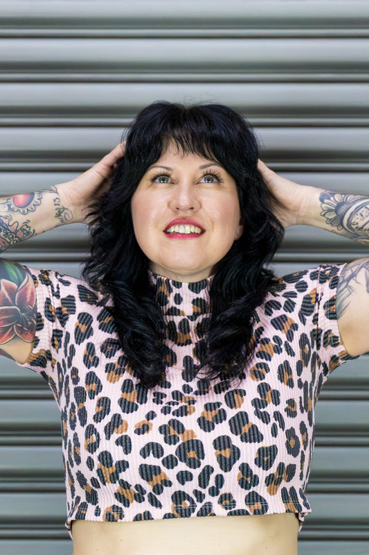 Person wearing a leopard print top with tattoos on arms against a metallic background