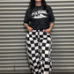 Person wearing a black t-shirt with graphic design and checkered pants standing in front of a metallic shutter.