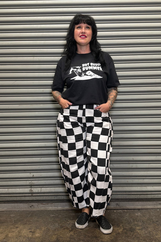 Person wearing a black t-shirt with graphic design and checkered pants standing in front of a metallic shutter.