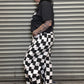 Person wearing a black t-shirt and checkered pants standing against a metal shutter.