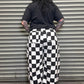 Person wearing a black t-shirt and checkered pants standing in front of a metal shutter.