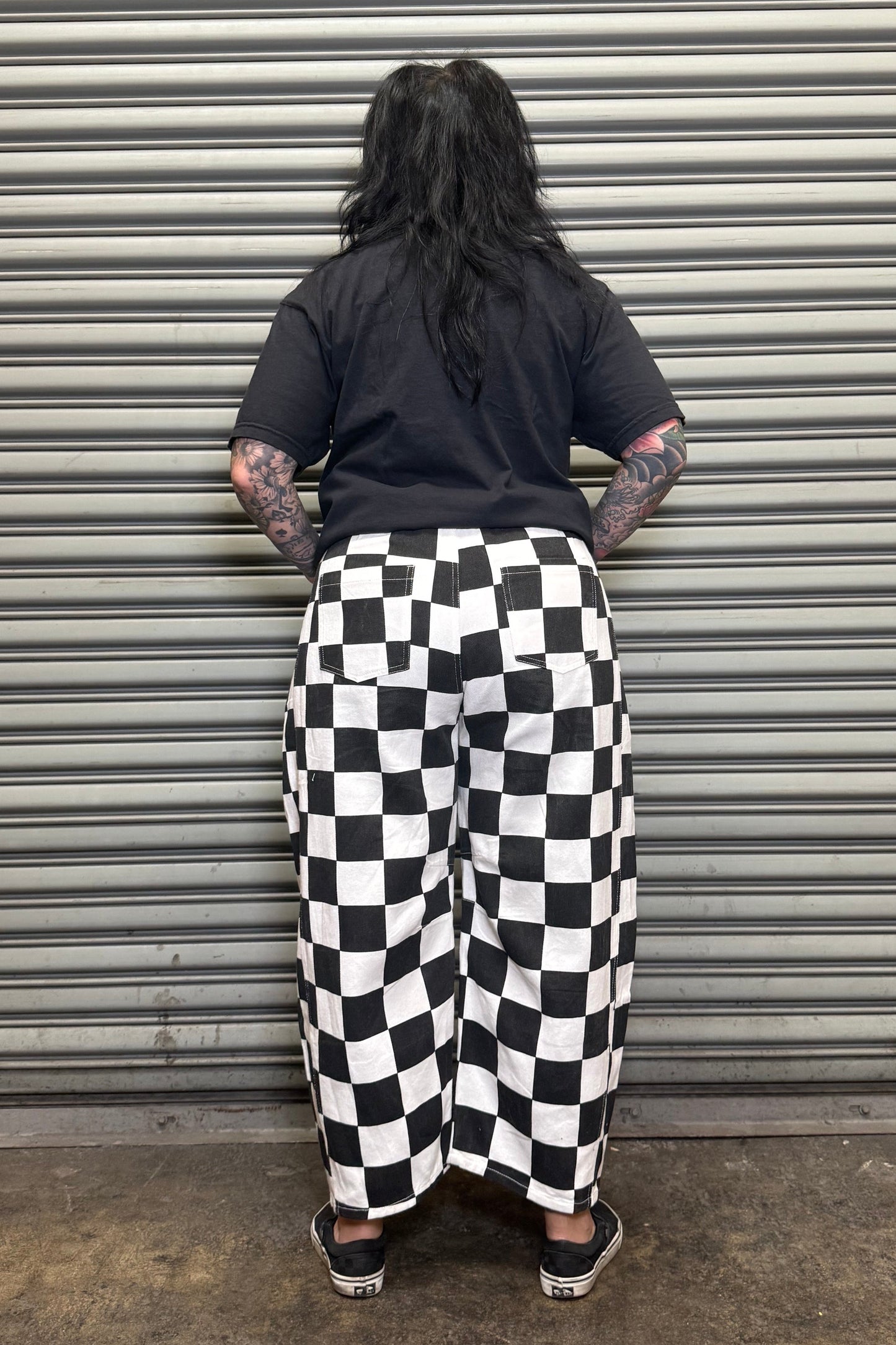 Person wearing a black t-shirt and checkered pants standing in front of a metal shutter.