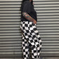 Person wearing a black and white checkered outfit standing in front of a metal shutter.
